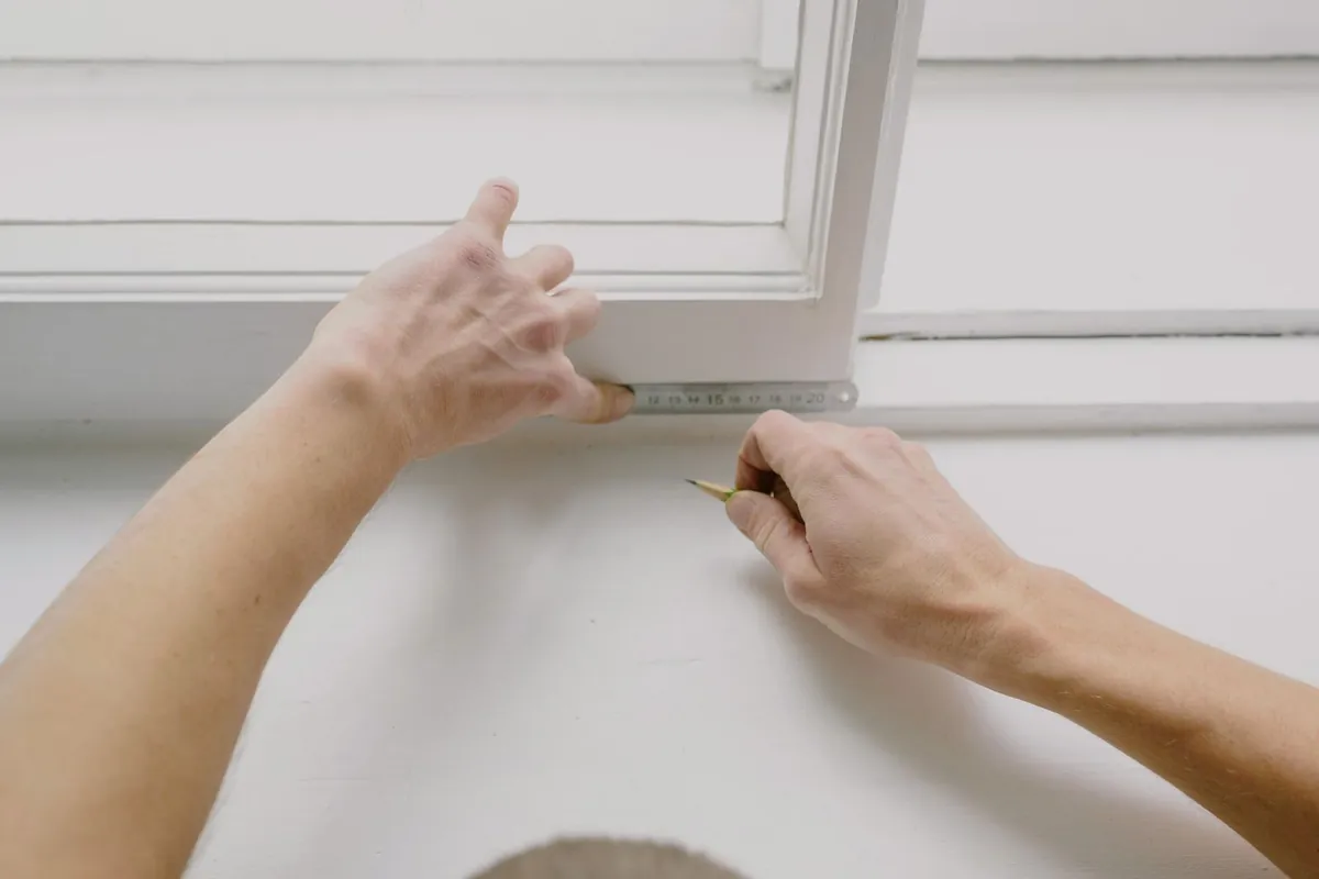 Close-up of hands working along the edge of a white window frame